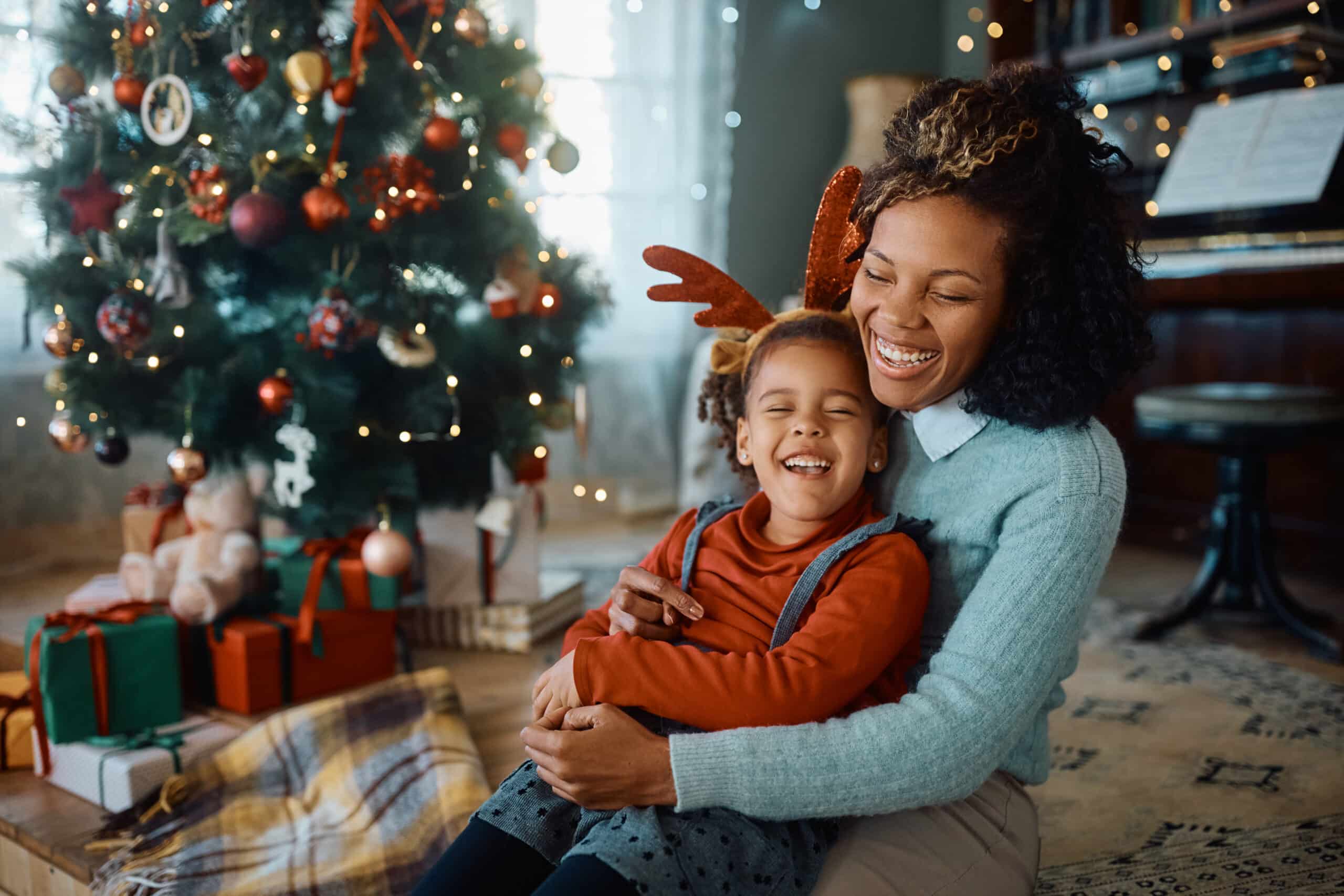Joyful black mother and daughter laughing on Christmas day at home.
